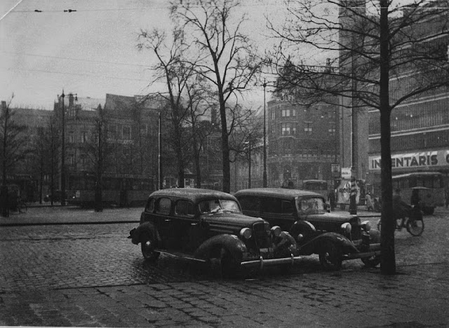 black and white photo of 1950s cars parked on a cobblestone street
